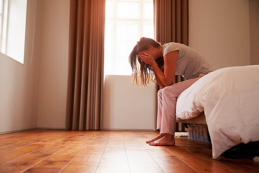 person sitting on bed with head in hands